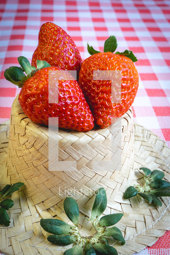 Fresh strawberries decorated on a straw hat. on a red picnic blanket.