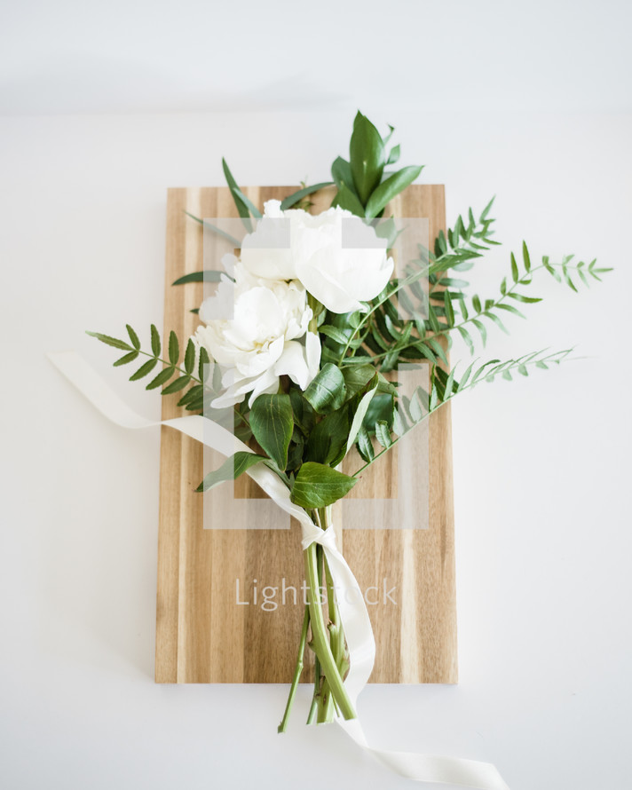 White flowers and greenery tied together and laying on a wooden cutting board.