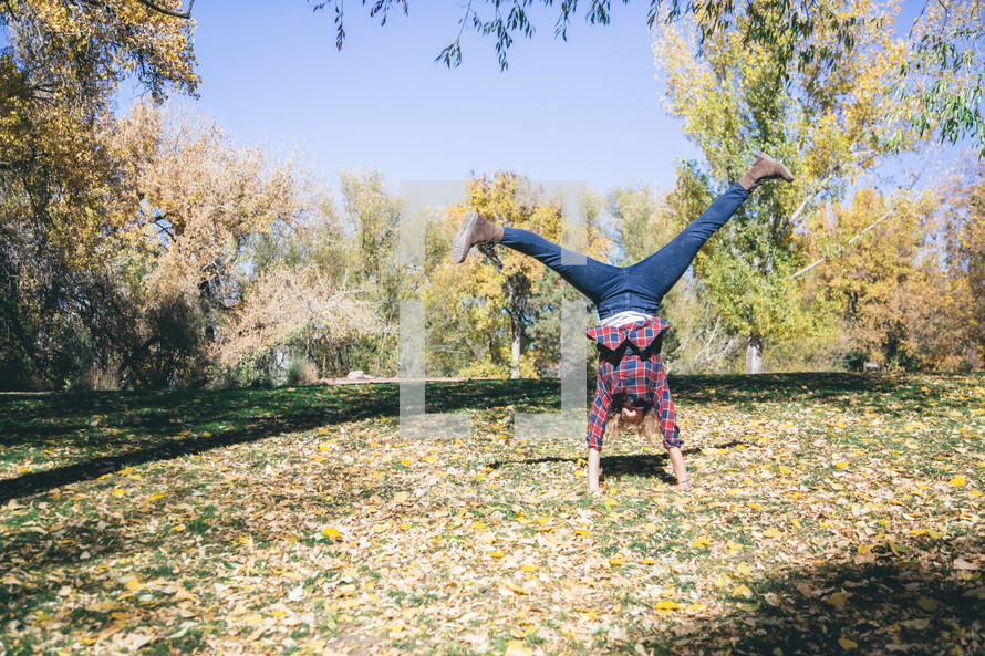 a woman doing a hand stand in fall leaves on the ground 
