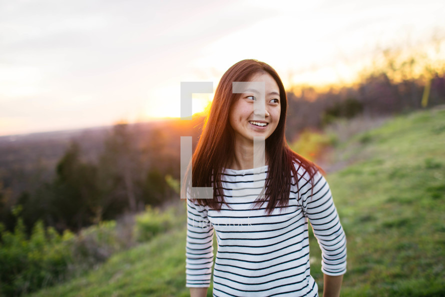 An Asian girl walking in a meadow at sunset 