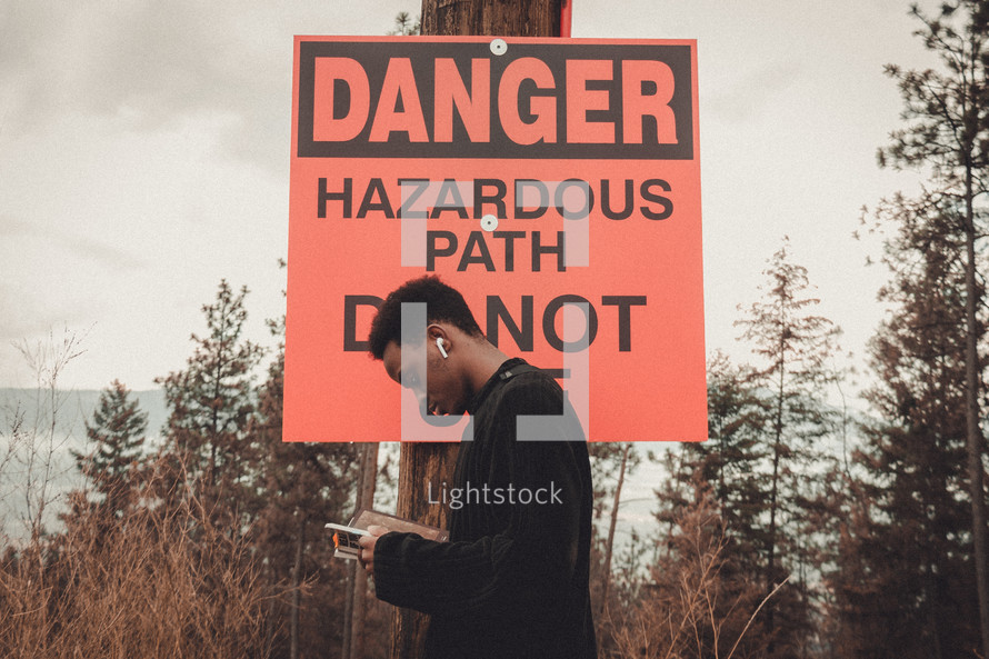 young man in front of a Dangerous Hazardous Path sign 