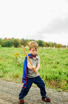 a boy in a cape holding a wooden sword 