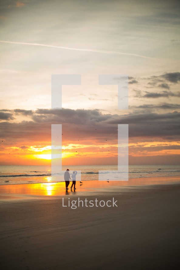 a couple walking on a beach at sunset 