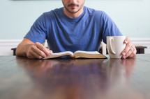 man reading a Bible holding a cup of coffee 