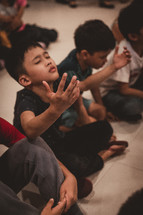 children sitting on the floor with raised hands 