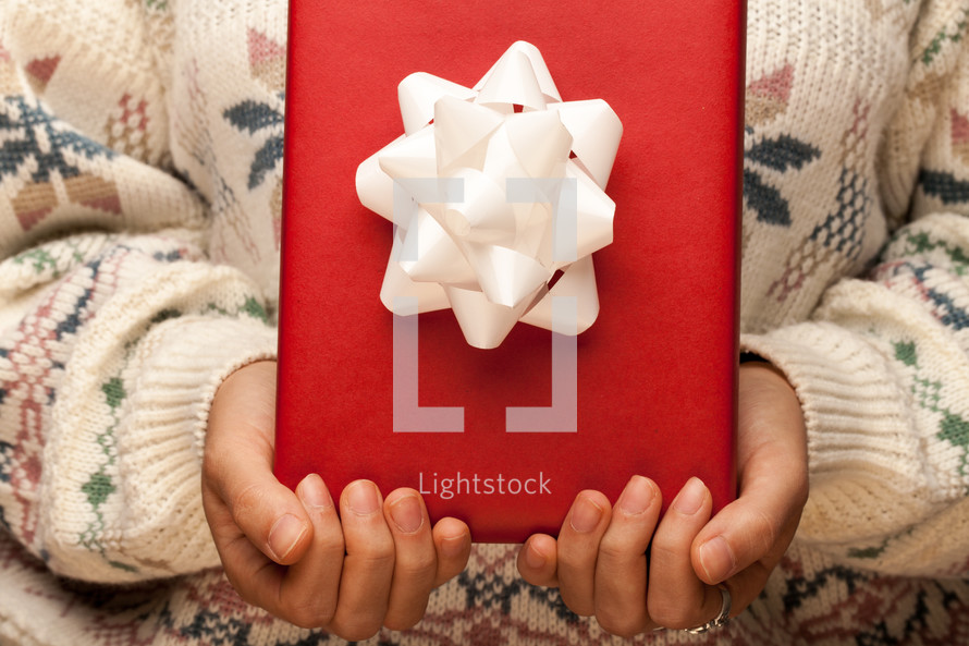 a woman in a sweater holding a wrapped Christmas gift 