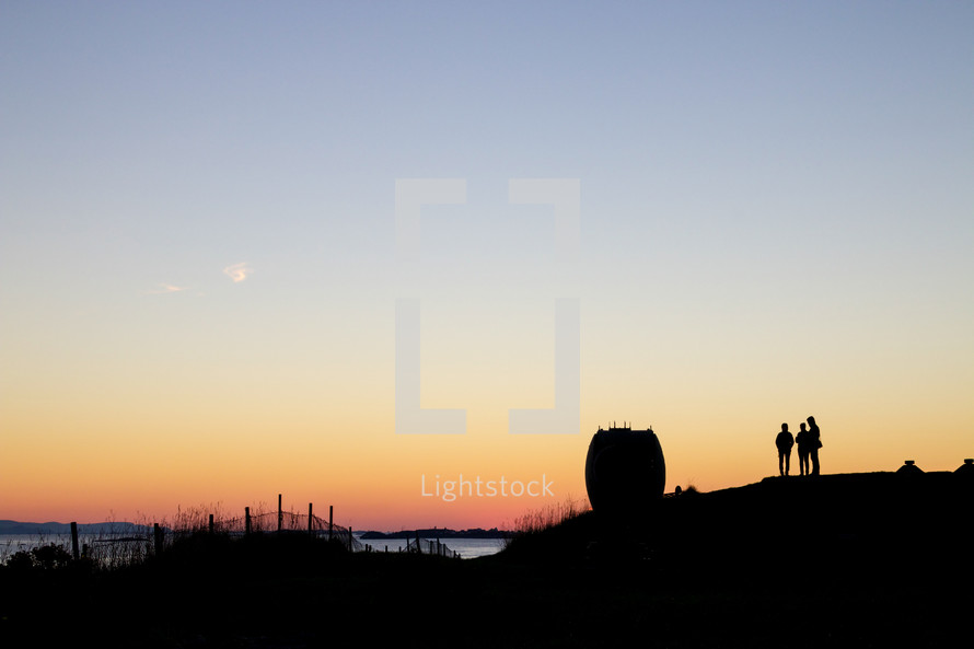 silhouettes of people standing on a shore at sunset 
