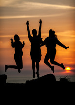 Three people jump for joy against a sunset in the background