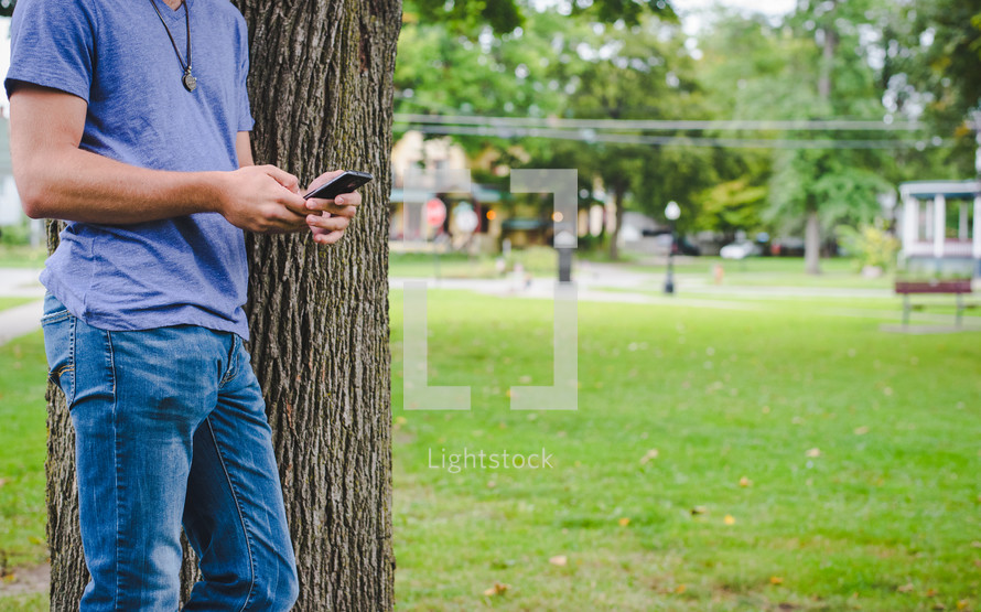 man texting beside of a tree