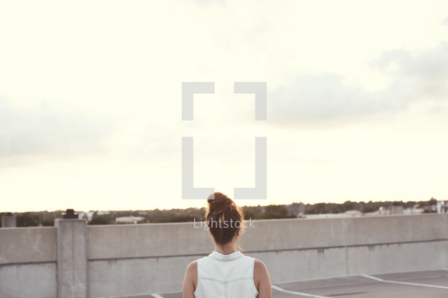 Back of a woman standing on a rooftop.