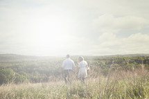 Couple walking through a field surrounded by hills.