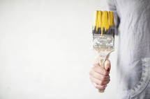 A woman holds a paint brush dripping yellow paint.