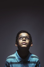 Young kid with glasses looking up.