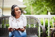 a young woman sitting on a porch reading a Bible 