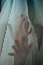 reaching hands through a sheer white fabric 
