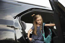 A little girl climbing out of the back seat of a car.