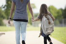 a young girl holding hands with mom walking to school 