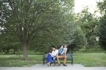 family sitting on a park bench outdoors 