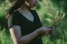a young woman standing in a field holding grains of wheat 