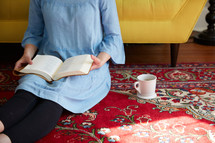 a woman sitting on a rug reading a Bible 
