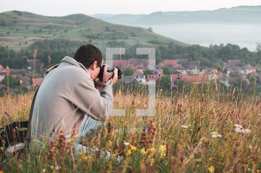 man with a camera taking pictures of a town in a valley 