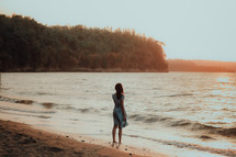 a young woman standing on a shore at sunset 