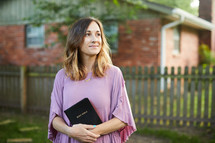 a woman holding a Bible standing outdoors 