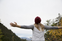 woman standing outdoors on a mountain with outstretched arms 