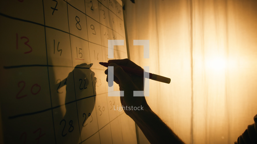 Silhouette of hand marking important date on the calendar