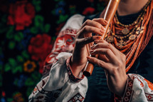 Hands of woman playing on woodwind wooden flute - ukrainian sopilka on colorful background. Folk music concept. Musical instrument. Musician in traditional embroidered shirt - Vyshyvanka