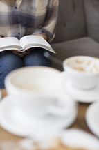 woman sitting on a couch reading and coffee cups 