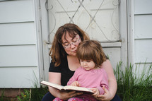 mother and daughter reading a Bible together outdoors 
