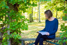 a woman sitting on a bench outdoors reading a Bible 