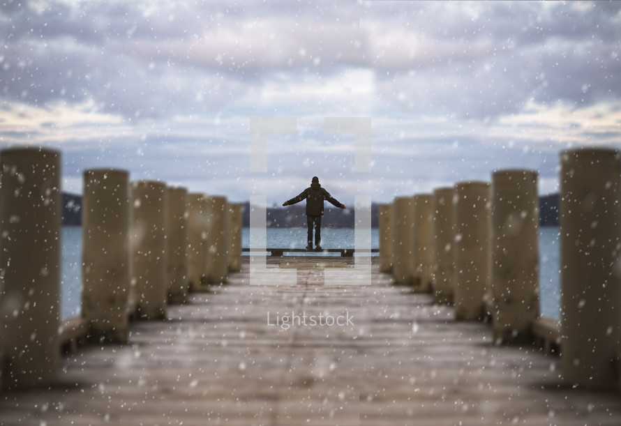 person standing at the end of a dock under falling snow 