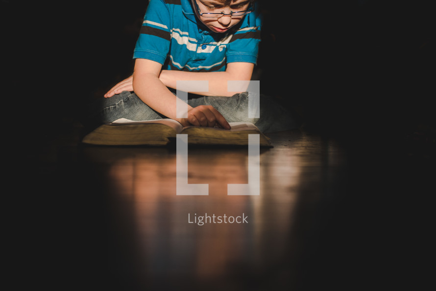boy reading a Bible on a wood floor 
