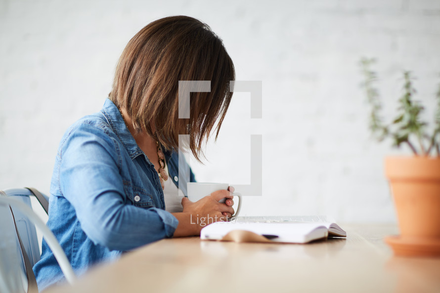 a woman holding a coffee mug and praying over a Bible 