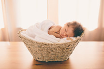 A newborn baby asleep in a basket.