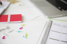 push pins and a planner on a desk 