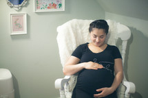 a pregnant woman holding her belly sitting in a rocking chair 