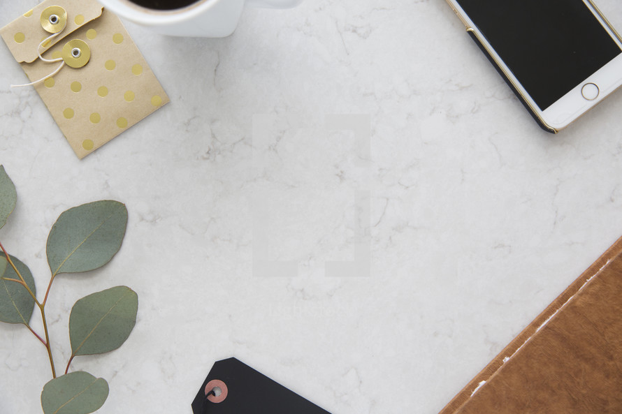 eucalyptus leaves, tags, coffee mug, iPhone, and journal on a desk 