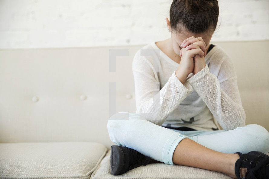 a girl sitting on a couch praying 