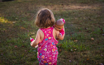 toddler girl carrying a baby doll 