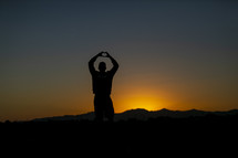 teen boy standing in warm sunlight making a heart shape with his hands 