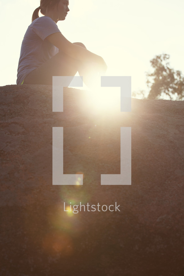 woman sitting on top of a rock under sunlight