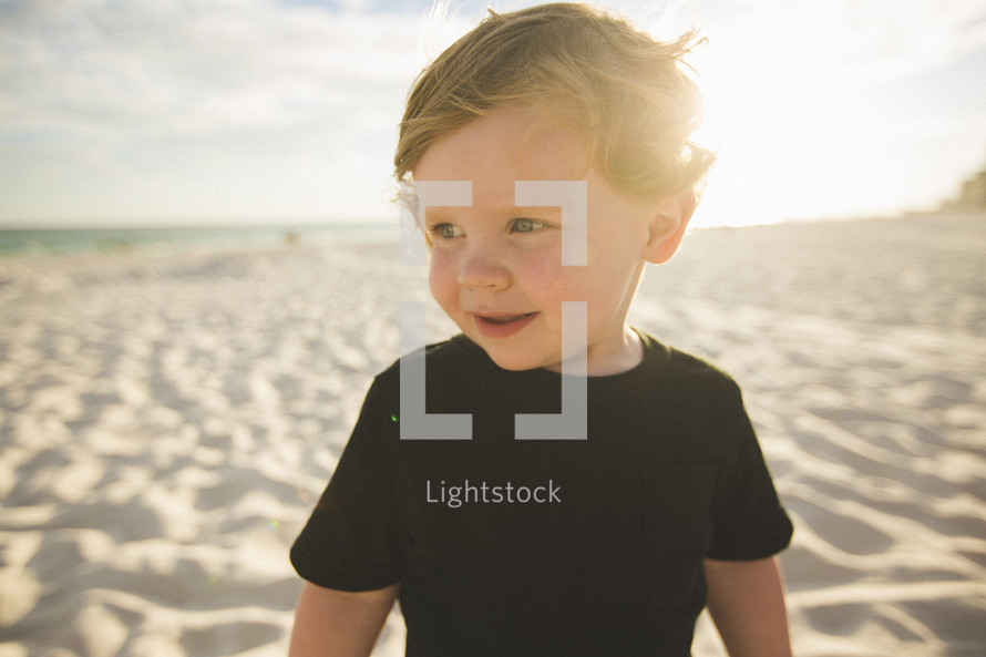 toddler boy standing on a beach 