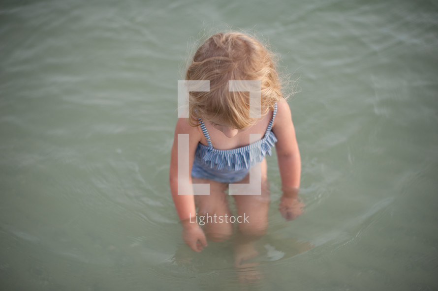 girl child in a bathing suit standing in water 