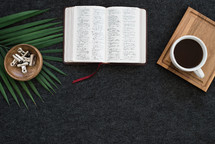 bowl of clips, palm fronds, Bible, watch, tray, and coffee mug on a desk 