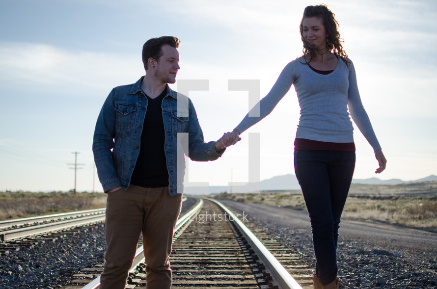 couple walking holding hands on railroad tracks 