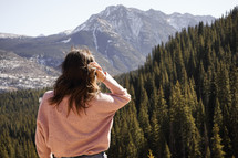 a woman looking out at an evergreen forest 