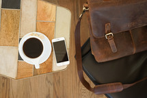 leather computer bag in a chair and iPhone and coffee mug on a table 